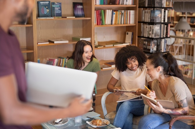 A diverse group of college students sitting together in a library, using laptops and textbooks to research college accreditation information. The setting is bright and collaborative, with students engaged in discussion.