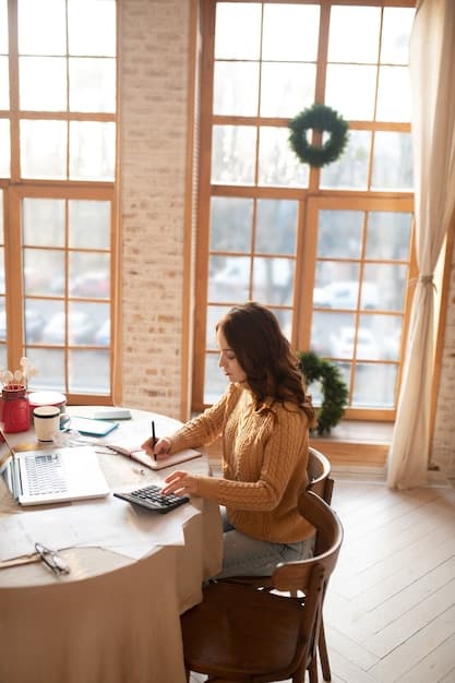 A person sitting at a desk reviewing mortgage documents and using a calculator. The scene is lit with natural light from a nearby window.