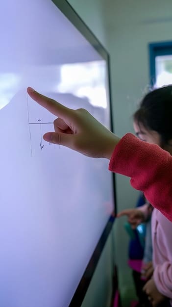 A close-up of a teacher's hands pointing at a digital whiteboard displaying the new education standards. The focus is on the teacher's interaction with the technology, emphasizing the integration of digital tools, with a few students visible in the blurred background, showing engagement.