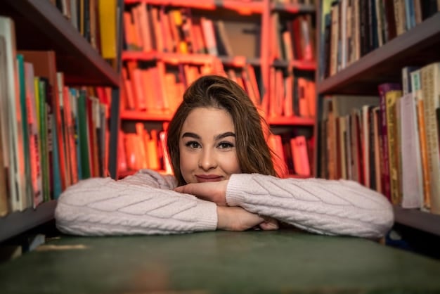 A close-up shot of a student studying in a university library, surrounded by books and research materials, with sunlight streaming through a large window, highlighting the focused academic environment.