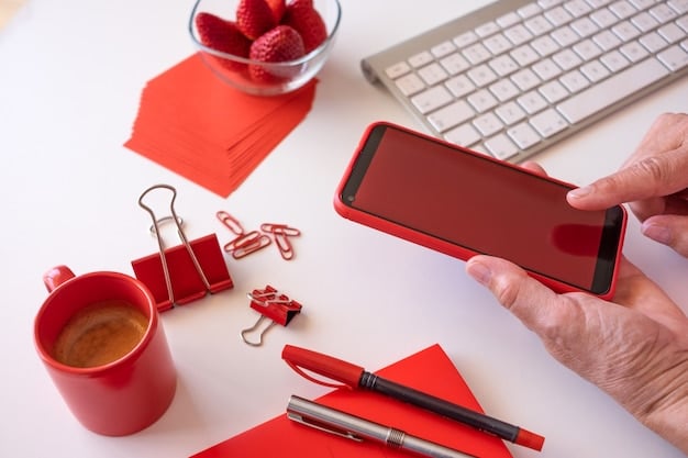 A hand crossing out items on a list of subscriptions with a red marker, on a wooden desk with other bills and a tablet showing a budget app.