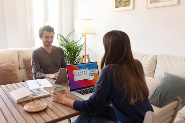 A friendly housing counselor assisting a person with completing an online housing assistance application on a laptop. The setting is a community resource center with other people working on computers in the background.